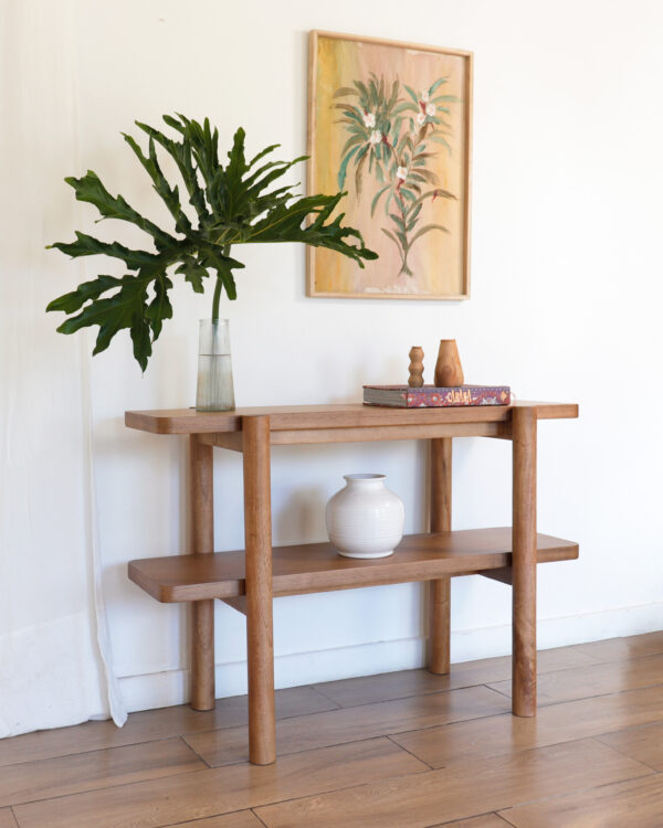 Consola Madrid minimalista de madera kiri, vista en ángulo, con estante inferior y decoración de jarrón blanco y libros.