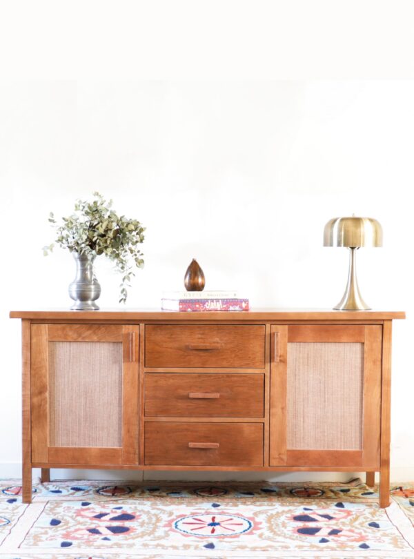 "Aparador Bali Bajo en madera de lenga con paneles de rafia, estilo sudeste asiático y clásico, ambientado con lámpara metálica y jarrón decorativo.