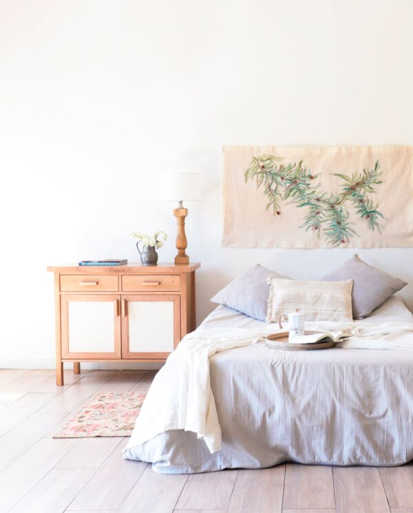 Cómoda Berna XS fabricada en madera kiri y rafia, estilo cálido, ubicada en dormitorio luminoso con cama y textiles neutros.