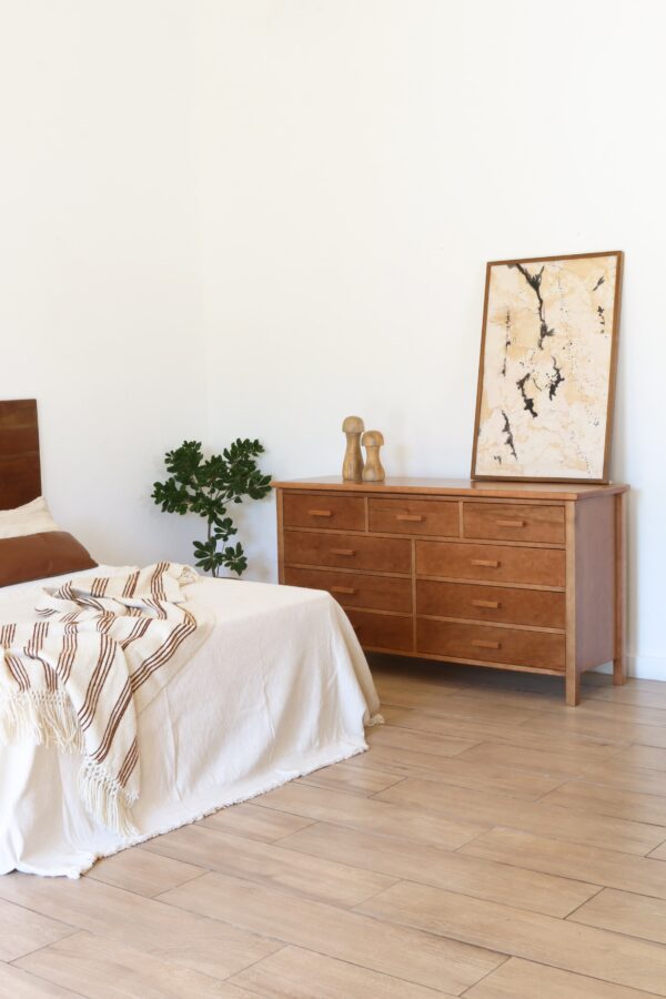 Cómoda Máximo de madera lenga estilo atemporal con ocho cajones, acompañada de decoración minimalista en un dormitorio moderno.