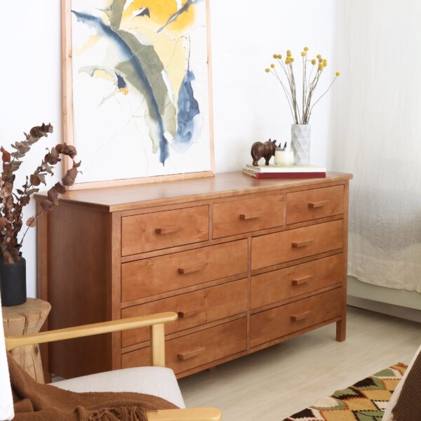 Cómoda Máximo de madera lenga estilo atemporal con ocho cajones, ambientada con cuadros y jarrón decorativo en sala de estar.