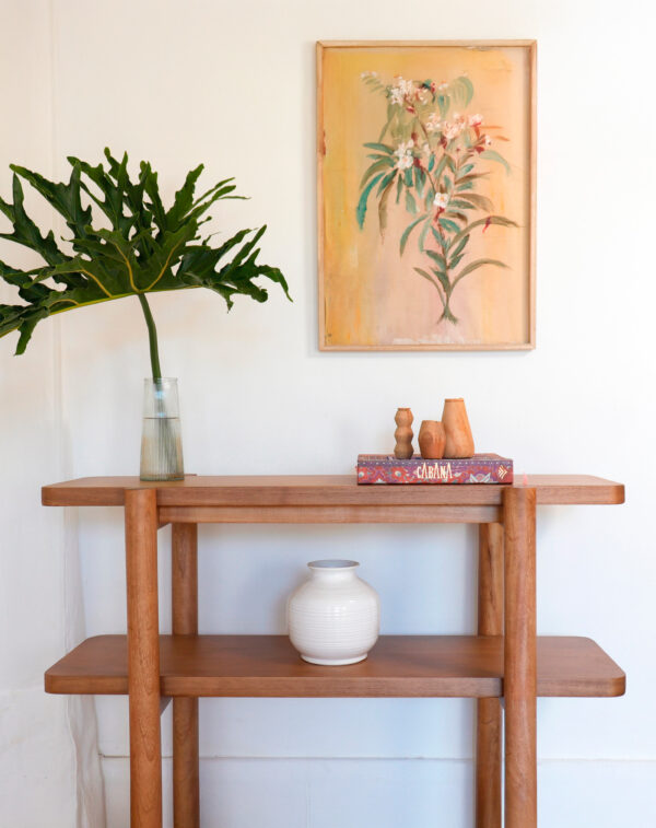 Consola Madrid de madera kiri en estilo minimalista, decorada con un cuadro de flores, jarrón blanco y libros sobre el estante superior.
