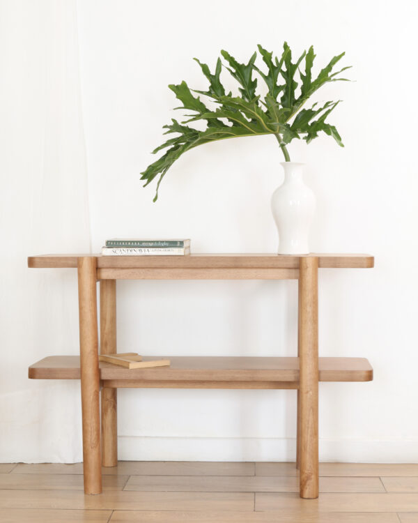Consola Madrid minimalista de madera kiri, vista frontal, con estante inferior y decoración de libros y jarrón blanco con hojas verdes.