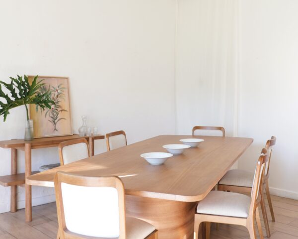 Vista en ángulo de la mesa Lanín en madera kiri estilo contemporáneo con seis sillas tapizadas y bowls blancos alineados