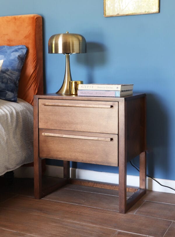Mesa de luz Madrid de madera oscura con tiradores lineales, combinada con una lámpara dorada moderna.