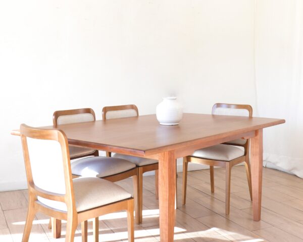 ista lateral de la mesa de comedor Máximo maciza en madera lenga estilo clásico con cuatro sillas tapizadas en color claro y un florero blanco sobre la superficie