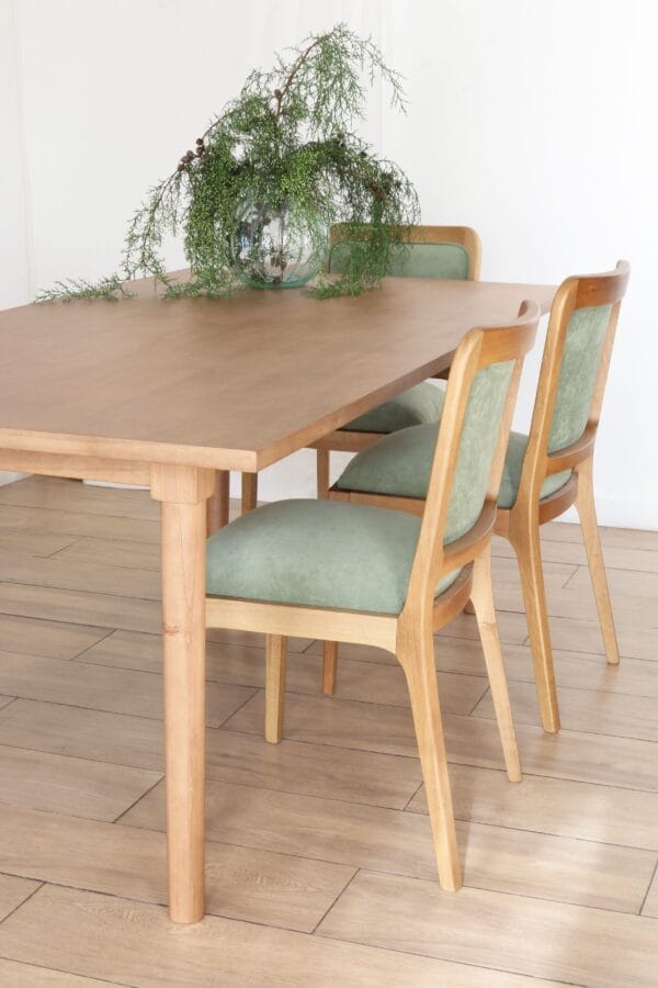Detalle de la mesa de comedor Madrid en madera kiri estilo nórdico con sillas tapizadas en verde y centro de mesa con follaje en jarrón de vidrio