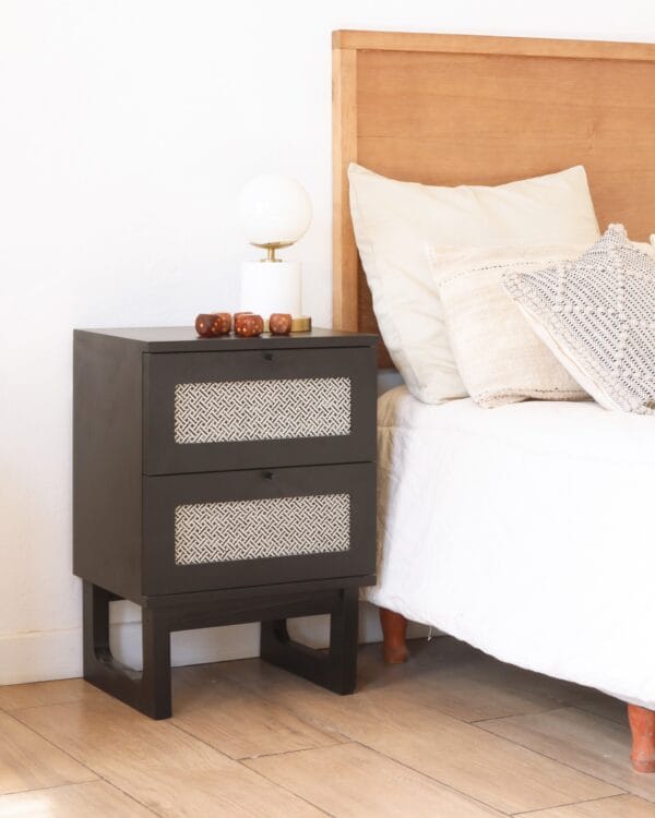 Mesa de luz Río fabricada en MDF color negro, con dos cajones y frente decorativo en tejido geométrico.