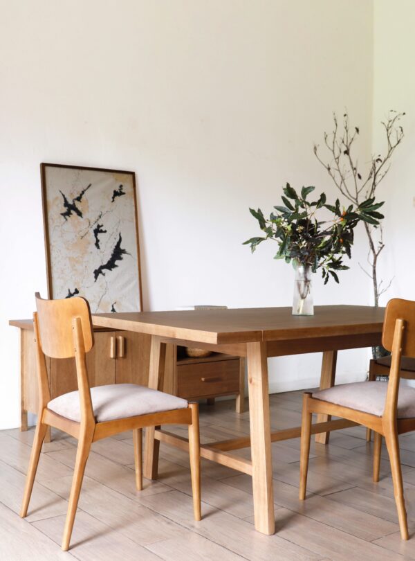 Detalle lateral de la mesa de comedor Oslo en madera kiri estilo hygge con sillas de respaldo curvo y asiento claro