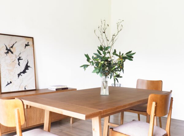 Mesa de comedor Oslo en madera kiri estilo hygge con cuatro sillas tapizadas y centro de mesa con jarrón de hojas verdes