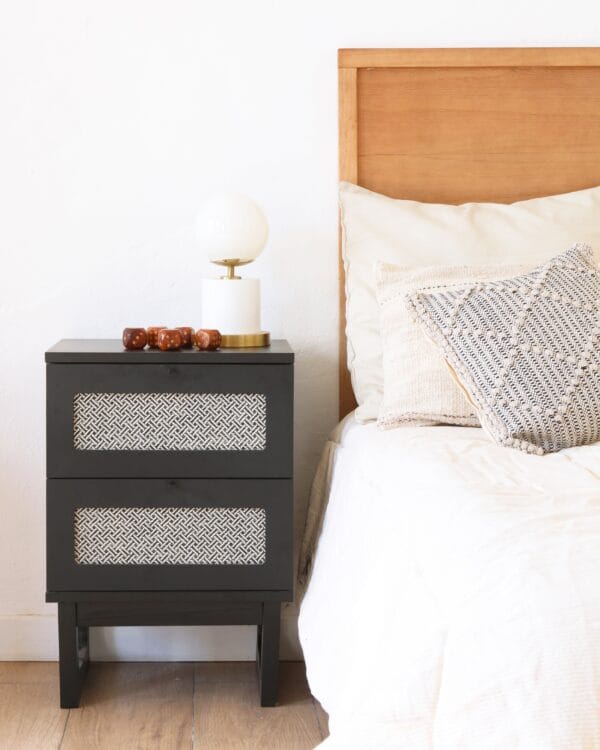 Mesa de luz Río de MDF en color negro con dos cajones y detalles tejidos, estilo moderno junto a la cama.