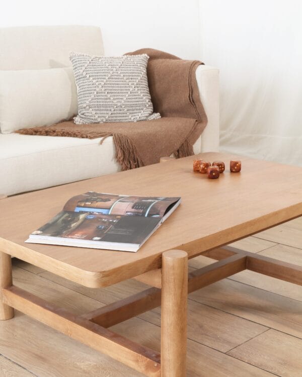 Mesa de living rectangular modelo Madrid Frente, en madera kiri, de estilo sobrio, ubicada frente a un sillón beige con manta marrón y almohadón tejido.