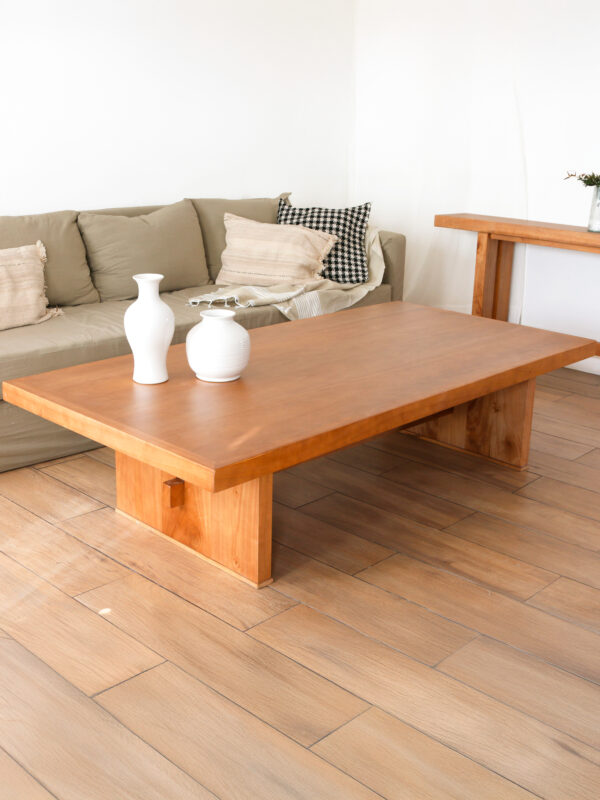 Mesa de living Nápoles de madera kiri, estilo elegante, con tapa amplia rectangular y base central maciza. Frente a un sillón beige con almohadones.