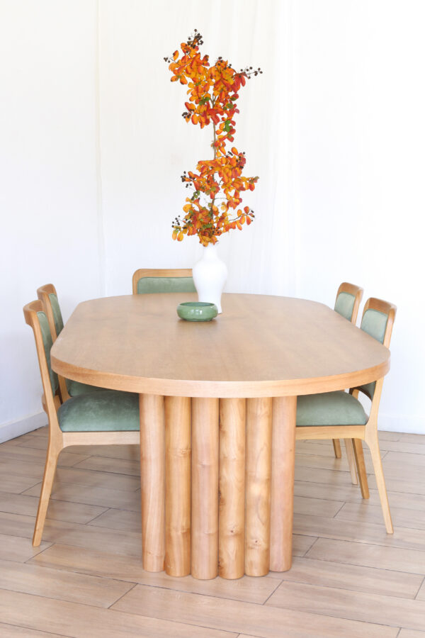 Mesa de comedor Nórdica en madera kiri estilo escultórico con cuatro sillas verdes y centro de mesa decorado con flores naranjas
