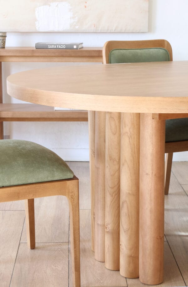 Detalle de la mesa Nórdica en madera kiri estilo escultórico con base cilíndrica tallada y silla tapizada en verde