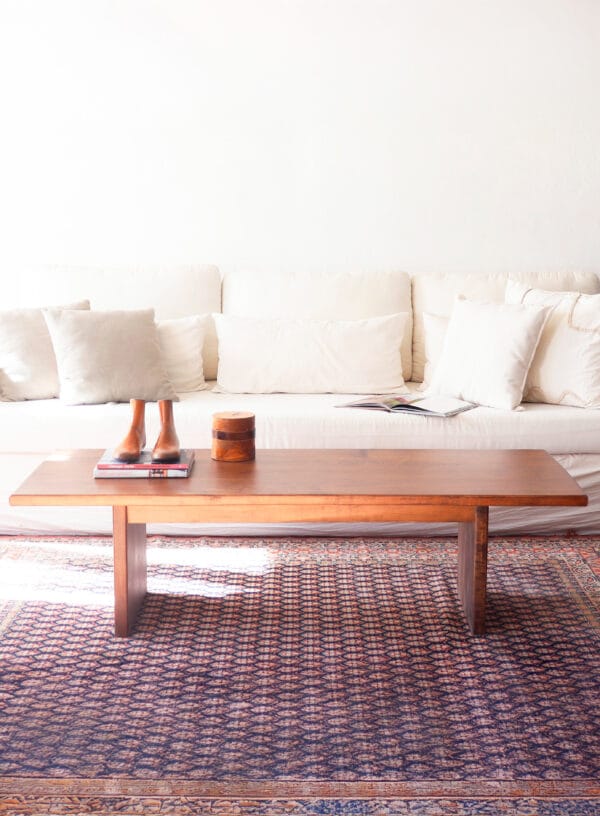 Mesa de living Urbana maciza de madera lenga, diseño contemporáneo, sobre alfombra con motivos geométricos frente a sillón blanco.