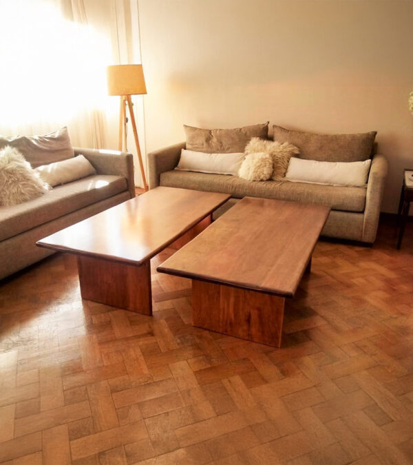 Mesa de living modelo Urbana con Marco Frente en madera maciza de lenga, compuesta por dos piezas rectangulares, acompañada de sofás beige y lámpara de pie, en un living cálido y acogedor.