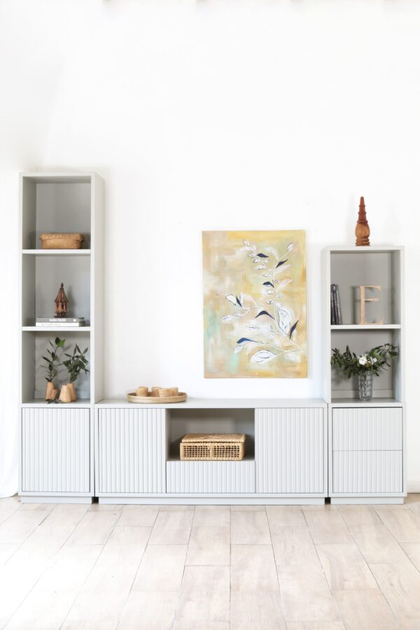 Modular Venecia Chico: mueble de salón blanco y gris claro con estantes, cajones y puertas acanaladas, ideal para almacenamiento y decoración moderna. Incluye obra de arte y detalles decorativos en madera.