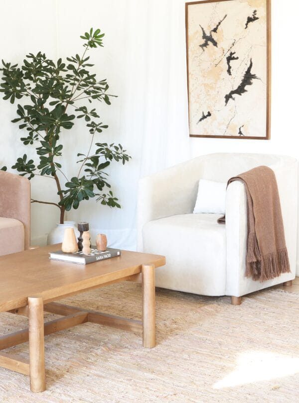 Poltrona London en tapizado beige con manta marrón, en una sala de estar moderna con mesa de centro de madera y planta.