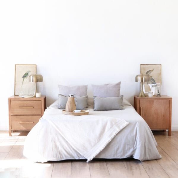 Dormitorio con cama de ropa clara, acompañada por dos mesas de luz de madera kiri modelo Provance Puerta, estilo clásico con líneas simples y lámparas metálicas sobre ellas.