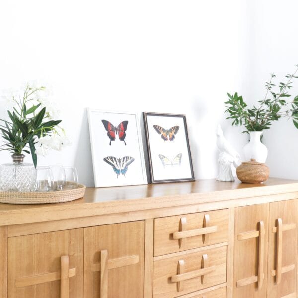 Aparador Provance de madera kiri estilo campiña francesa con adornos decorativos y cuadros de mariposas sobre la superficie.