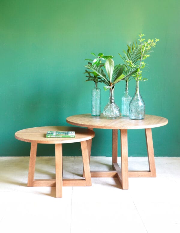 Set de dos mesas redondas Bjordal en madera kiri estilo minimalista, decoradas con botellas de vidrio y plantas.