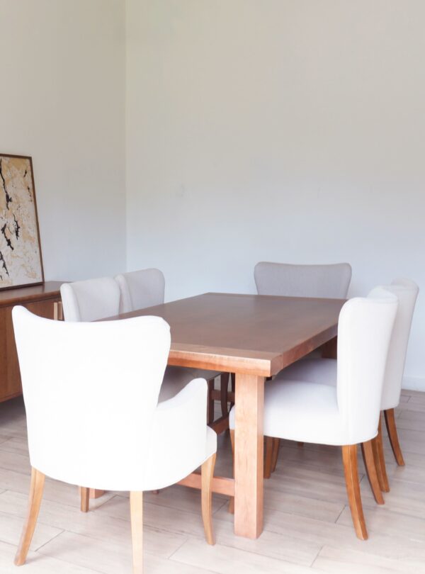 Conjunto de comedor con varias Sillas Oporto con brazo en guatambú, tapizadas en tono claro, acompañando mesa robusta de madera.