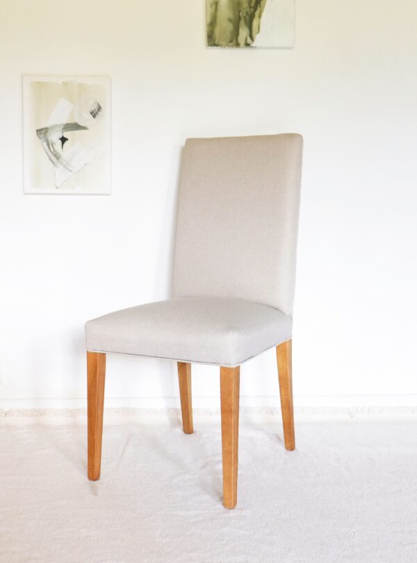 Silla vestida de comedor en madera de guatambú con funda en tono beige, estilo elegante, acompañando mesa rectangular de madera.