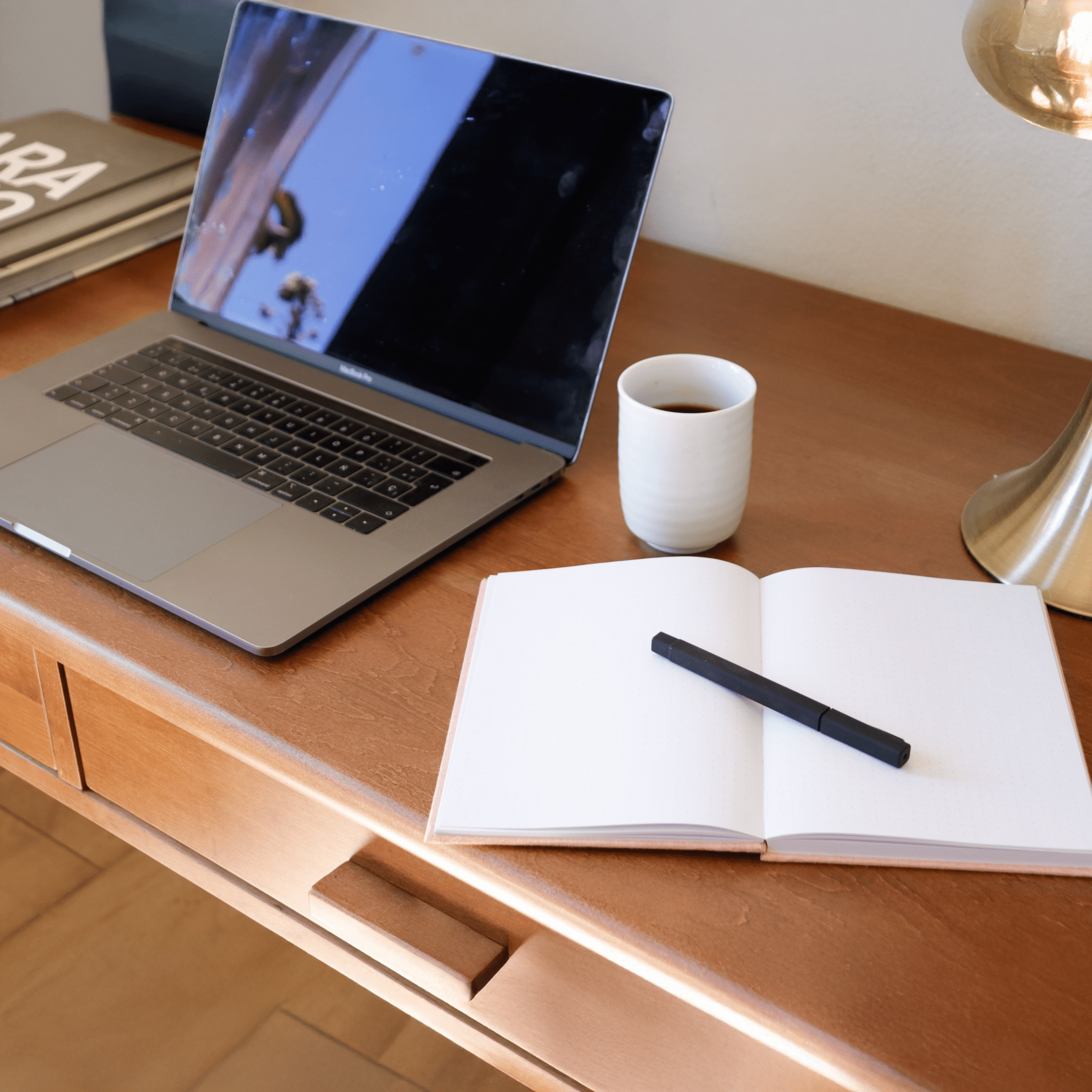 Escritorio de madera con portátil, taza de café, cuaderno abierto y bolígrafo.