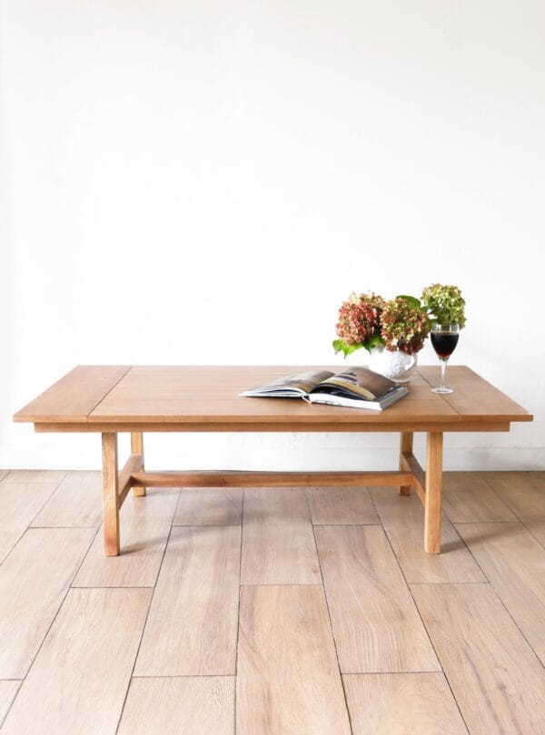 Mesa de centro Estocolmo en madera kiri, diseño minimalista rectangular, con líneas simples y detalles sutiles, acompañada de un florero con hortensias y un libro abierto.
