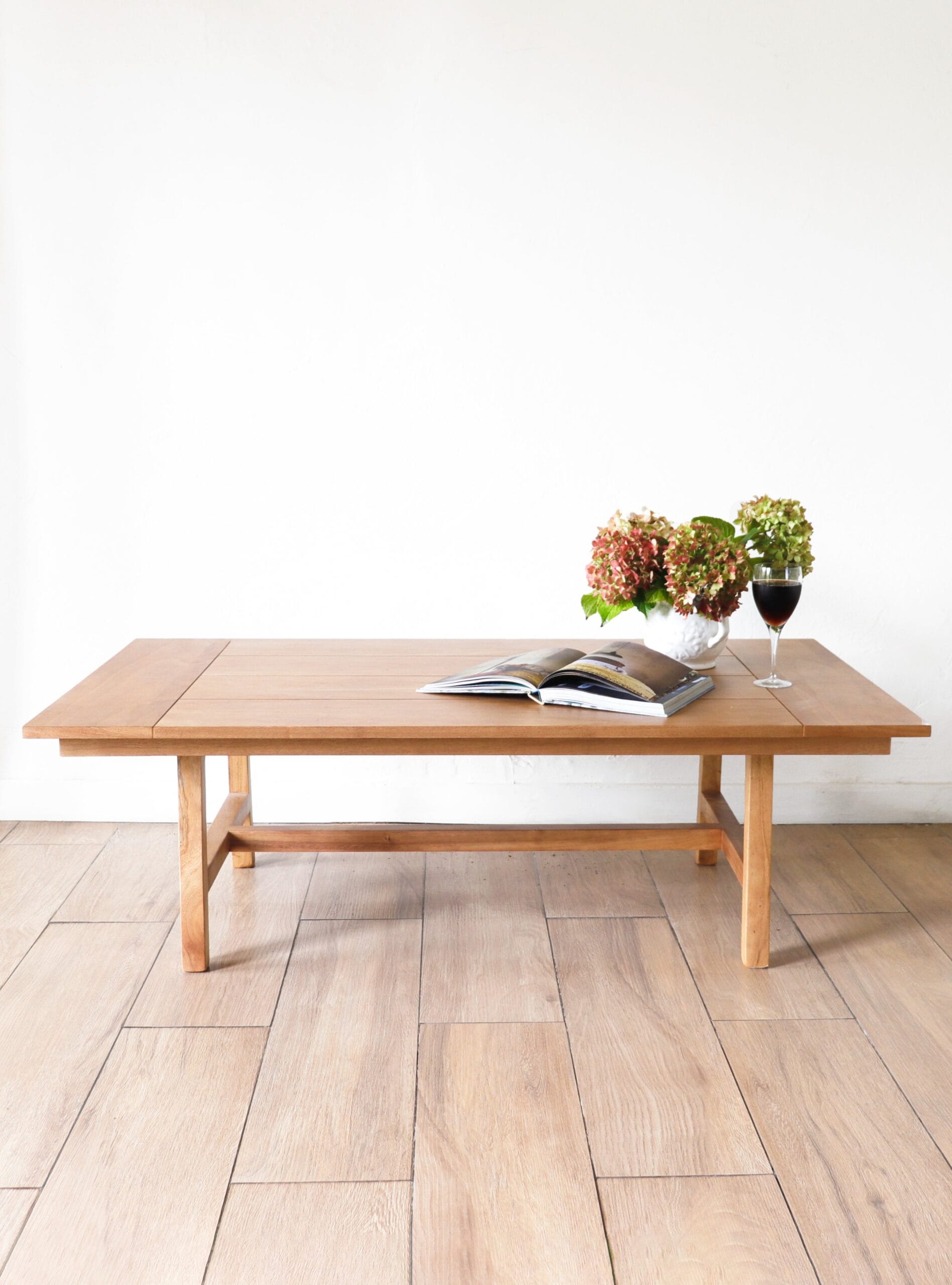 Mesa de centro Estocolmo en madera kiri, diseño minimalista rectangular, con líneas simples y detalles sutiles, acompañada de un florero con hortensias y un libro abierto.