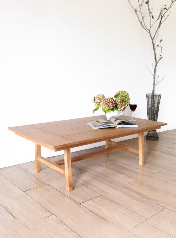 Mesa de living modelo Estocolmo en madera kiri, estilo minimalista, de forma rectangular con superficie lisa y patas rectas, decorada con flores y una copa de vino sobre su tapa.