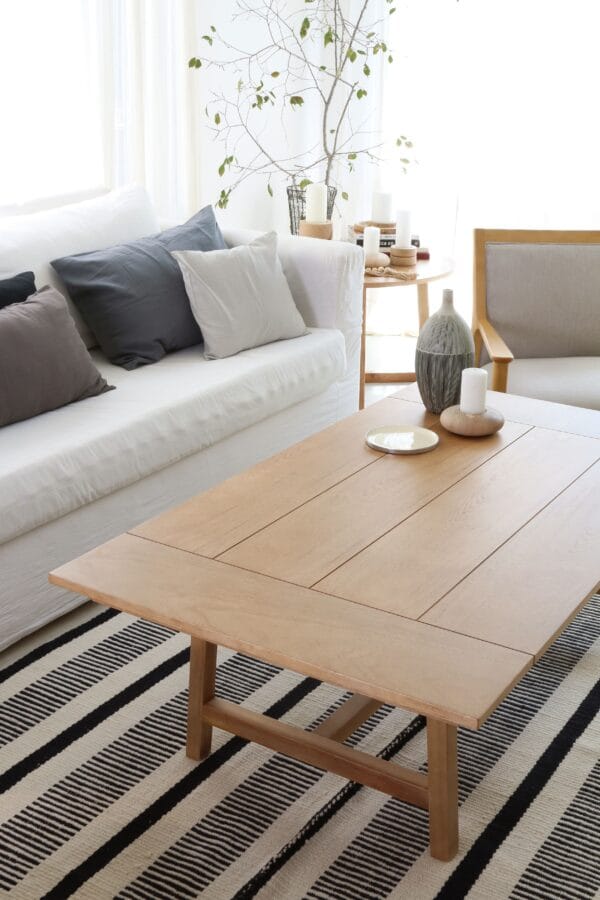 Mesa de living Estocolmo en madera kiri, estilo minimalista, ubicada en un ambiente luminoso con sofá blanco y sillón tapizado, sobre una alfombra rayada en blanco y negro.